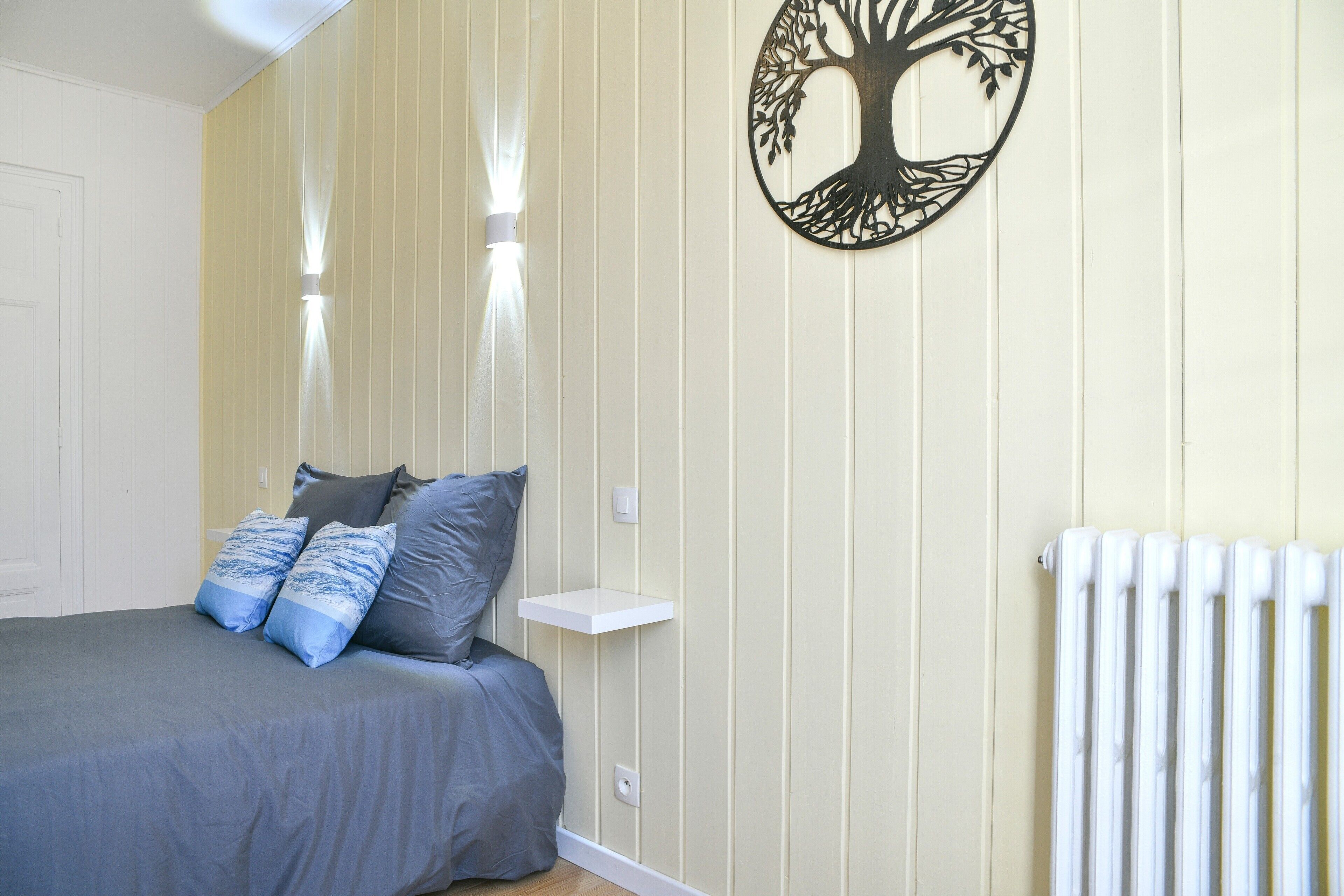 Un dormitorio con cama, almohadas, un estante en la pared, un radiador y una obra de arte colgada.