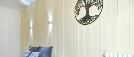 Un dormitorio con cama, almohadas, un estante en la pared, un radiador y una obra de arte colgada.