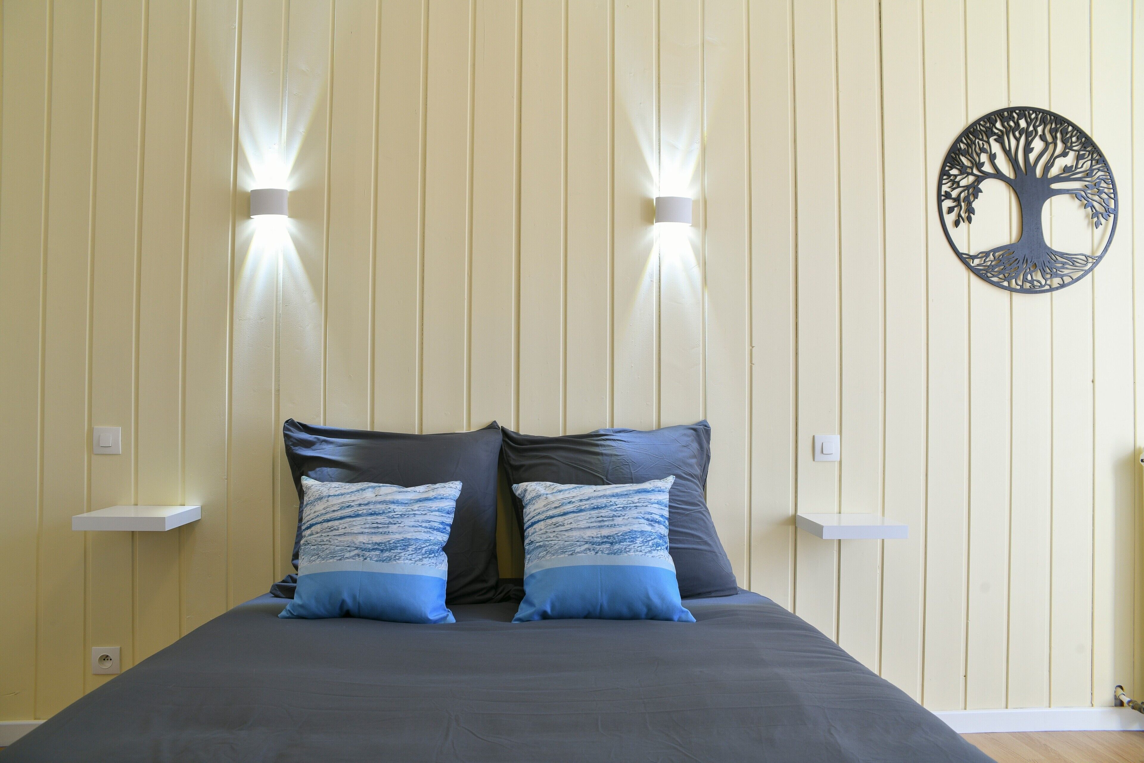 A bed with two pillows, a wall-mounted light fixture, and a tree-shaped decoration.