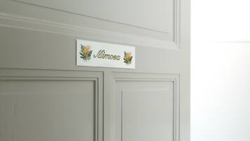 Une porte blanche avec une plaque portant le nom « Mimosa » et ornée de motifs de feuilles décoratives.
