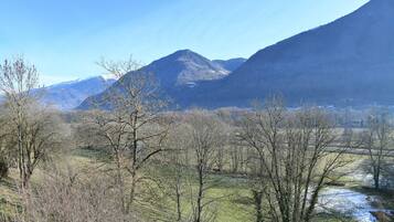 Eine gebirgige Landschaft mit Fluss, Bäumen und blauem Himmel.