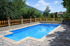 A rectangular swimming pool with a stone border, surrounded by a wooden fence and potted plants.