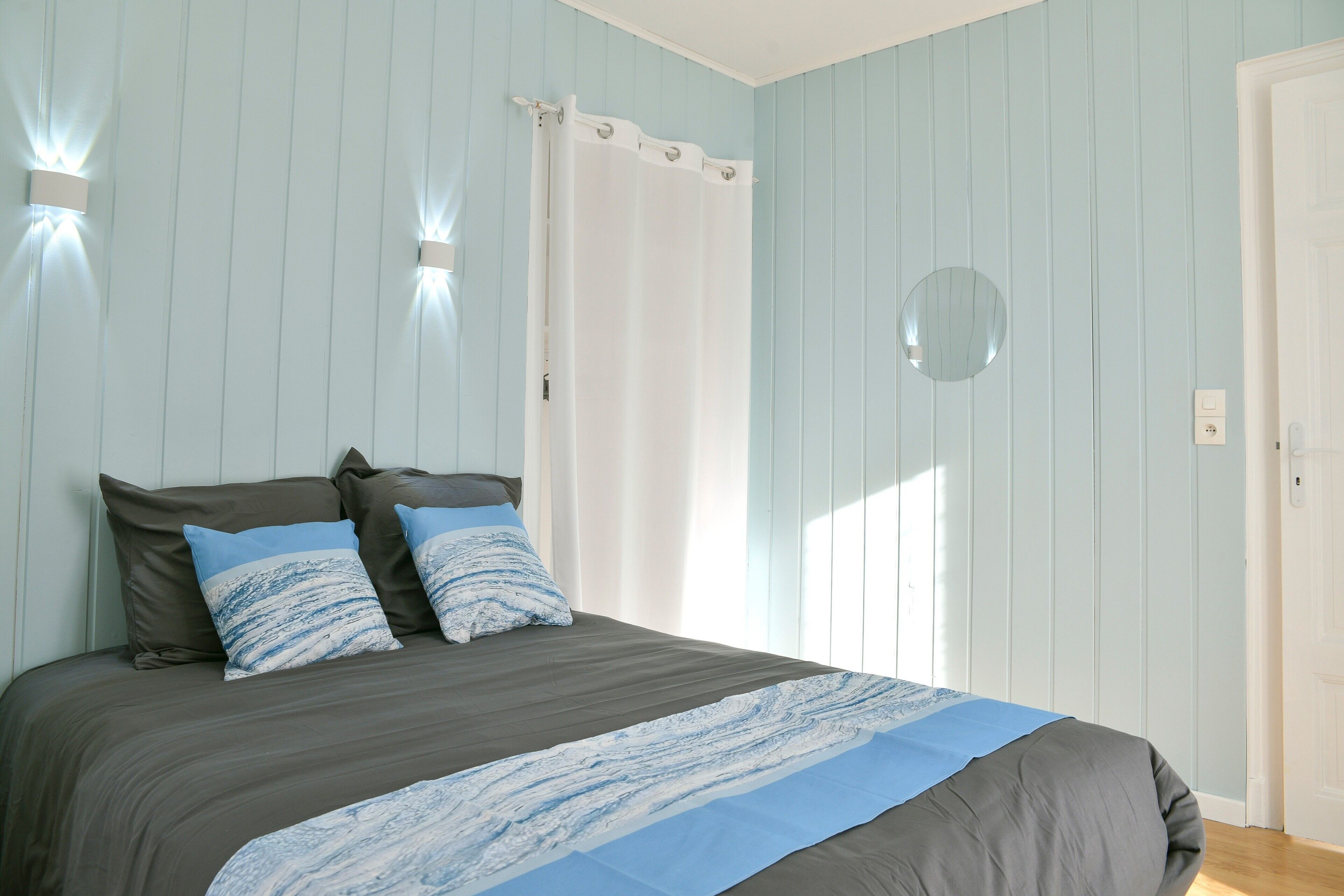 Une chambre à coucher avec un lit, des oreillers, un rideau, un miroir et une porte.