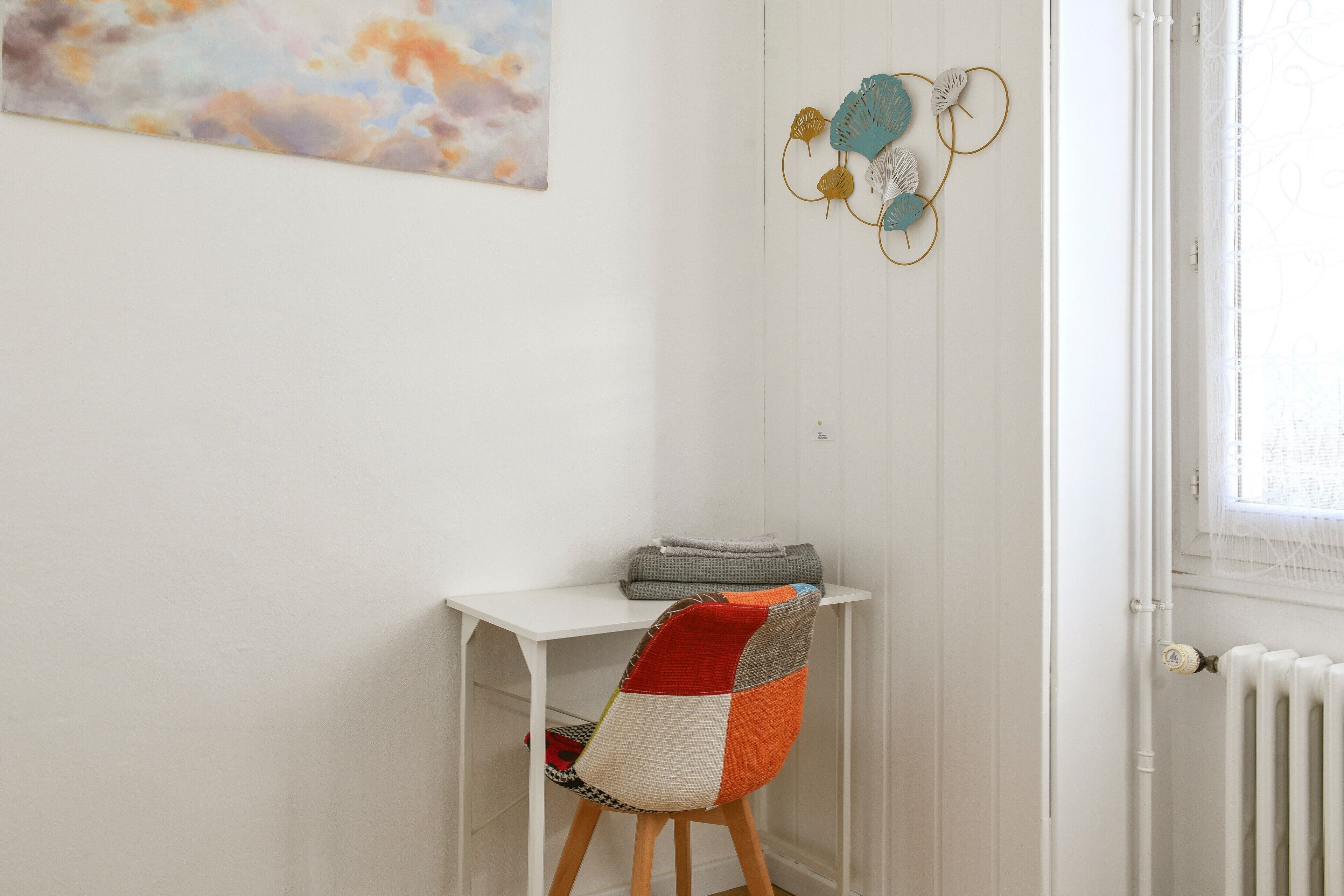 Een wit bureau met stoel, een radiator en een muur met een schilderij.
