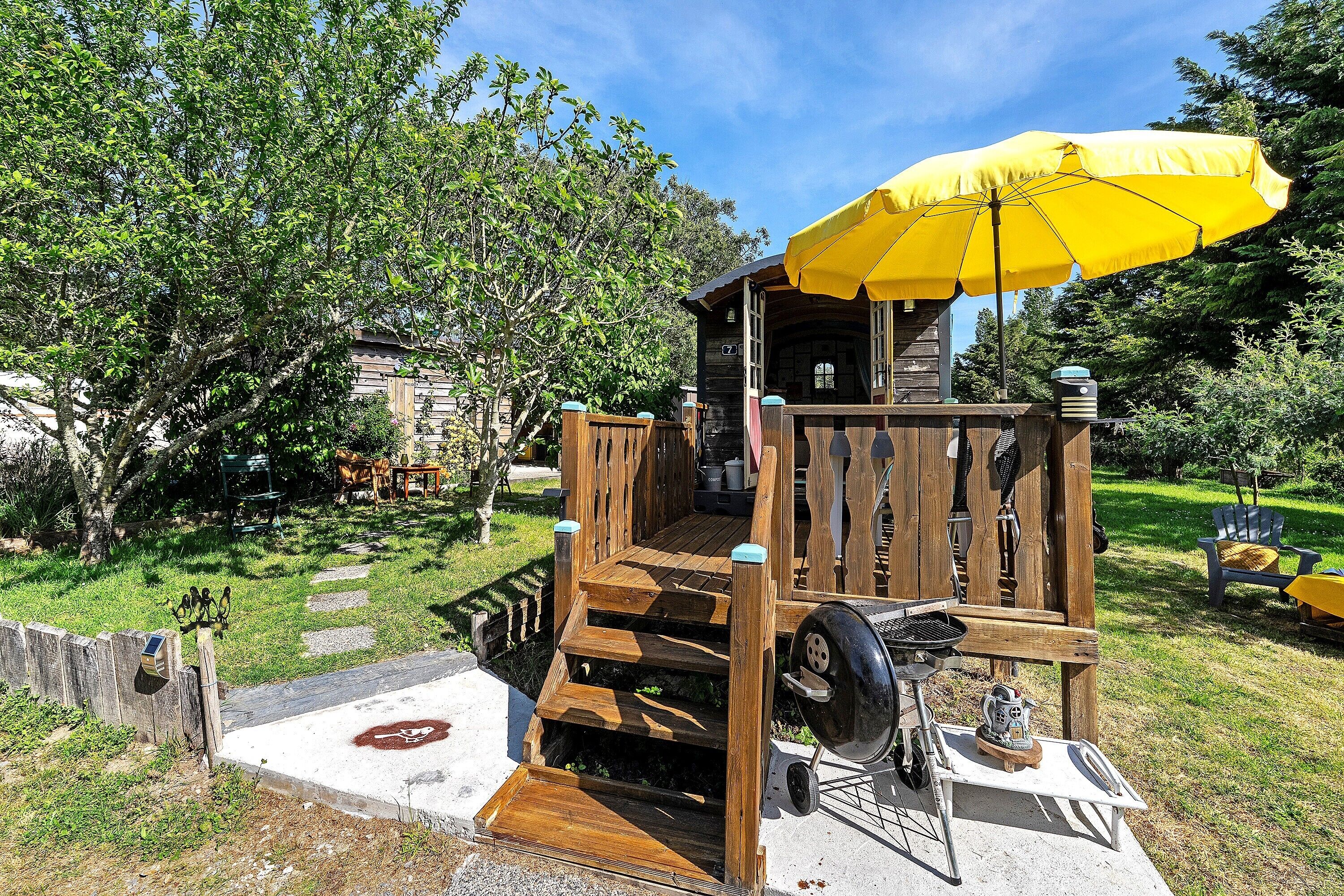 Een houten buitenconstructie met een gele parasol, trappen en een barbecue.