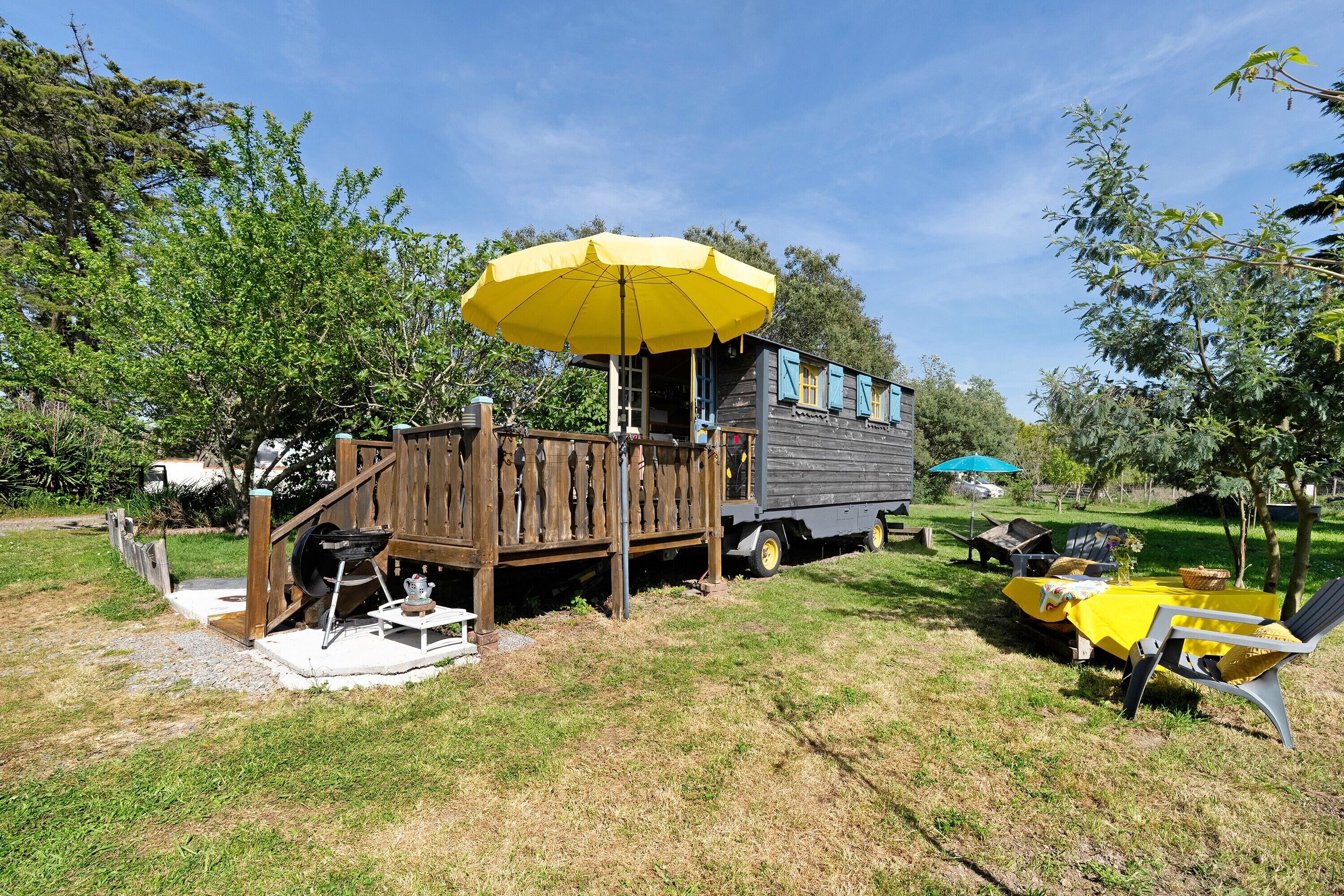 Une terrasse en bois avec un parasol jaune, une petite table et un espace barbecue.