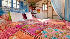 Uma cama com um edredom colorido, uma janela com cortinas e uma parede com um quadro.