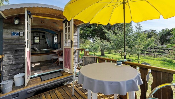 Uma cabana de madeira com varanda, uma mesa e um guarda-sol amarelo.