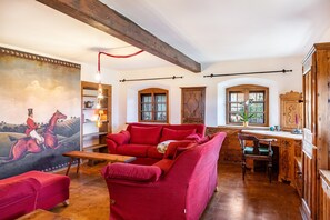 A room with a red sofa, wooden desk, and a painting of a horse rider.