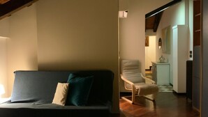 A room with a sofa, a chair, a lamp, and a view into another room with a kitchen area. - 'Ca' Molinetto' Apartment with Wi-Fi and Air Conditioning (Treviso)