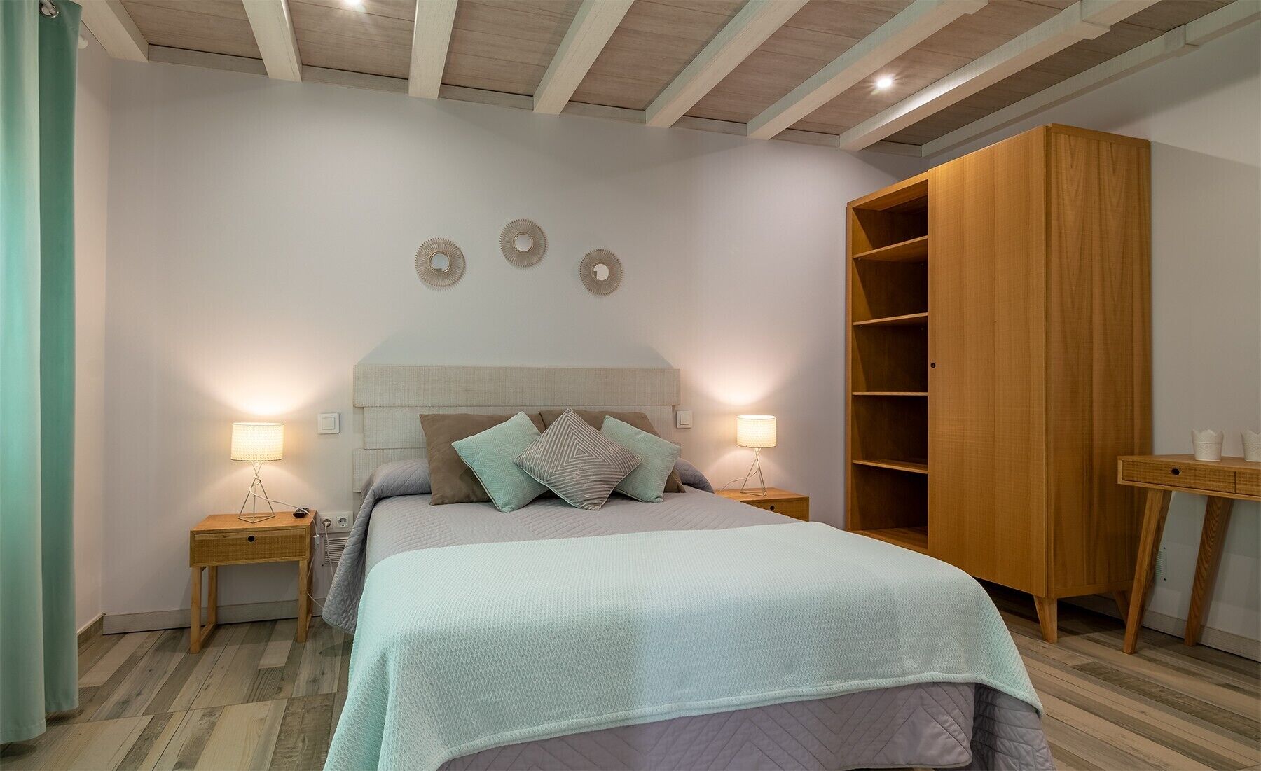 A bedroom with a bed, bedside lamps, a wardrobe, and a small table.