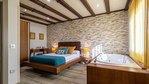 A bedroom with a stone wall, a wooden bed, a bedside table with a lamp, and a bathtub.