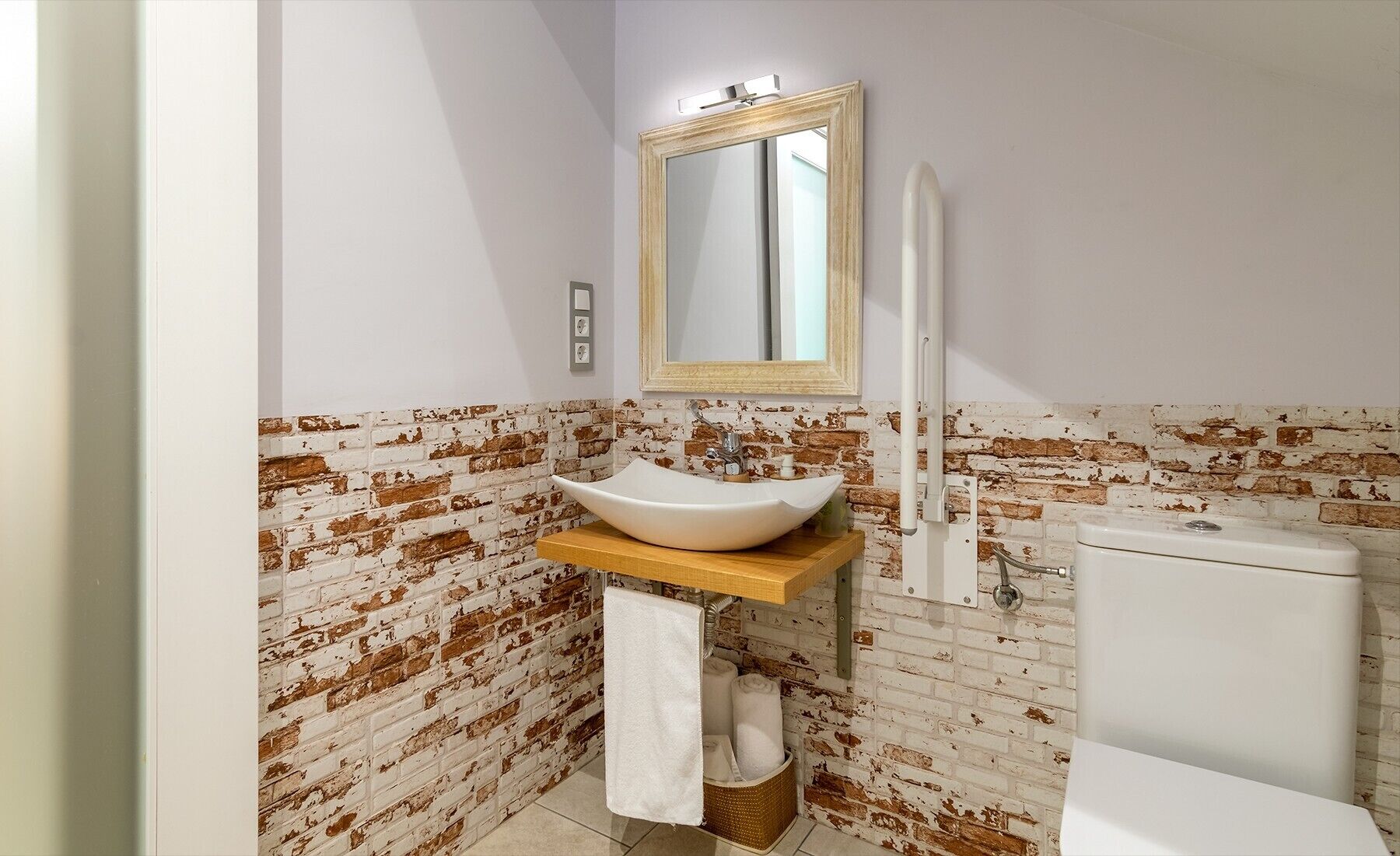 A bathroom with a white sink, a mirror, and a toilet against a brick wall.