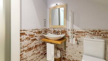 A bathroom with a white sink, a mirror, and a toilet against a brick wall.