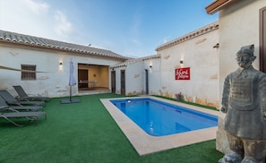 Un patio con piscina, sillas de descanso y una estatua.