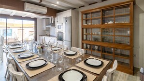 A dining area with a long table set for six, a kitchen in the background, and a display cabinet with glass doors.