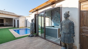 A pool with a glass door, a hot tub, and two statues.