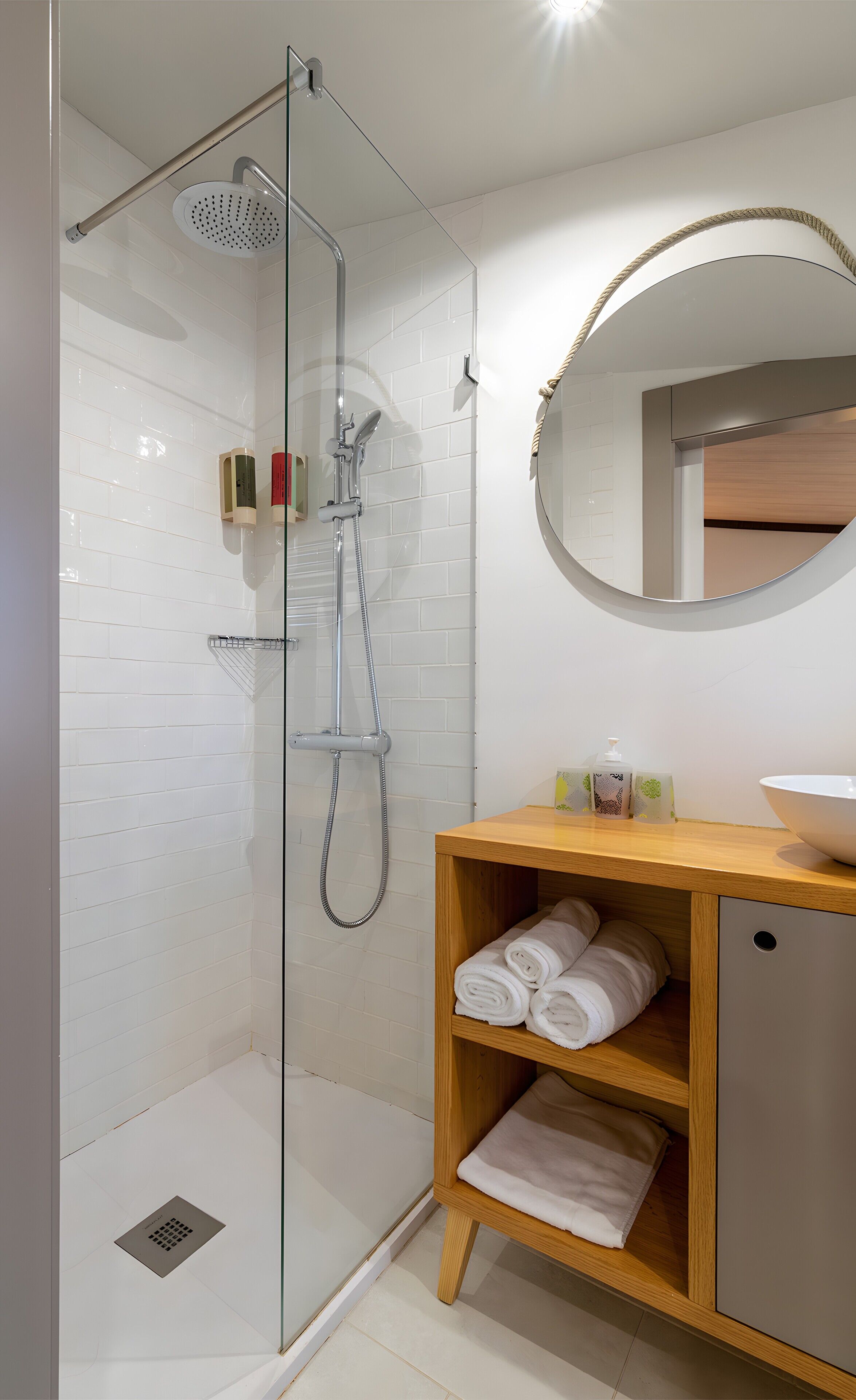 A modern bathroom with a glass shower enclosure, a wooden vanity with a mirror, and neatly folded towels.