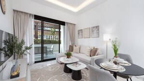 Ein modernes Wohnzimmer mit einer Couch, zwei Couchtischen, einem Esstisch für vier Personen und einem großen Fenster mit Vorhängen.
