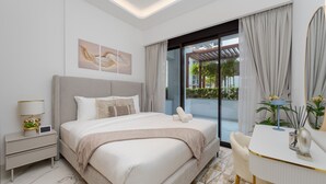 Ein modernes Hotelzimmer mit einem großen Bett, einem Nachttisch mit Lampe, einem Schreibtisch mit Stuhl und Blick ins Freie durch eine Schiebetür.