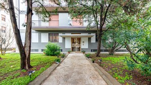 Un edificio con una entrada central, plantas en macetas y un camino de piedra que lleva a la entrada.