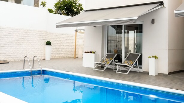 A swimming pool with two sun loungers, a covered seating area, and a white textured wall. - Casa Rafa - Villa 9 (Costa Adeje)