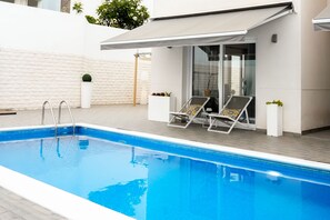 A swimming pool with two sun loungers, a covered seating area, and a white textured wall. - Casa Rafa - Private Heated Pool - Costa Adeje (Costa Adeje)