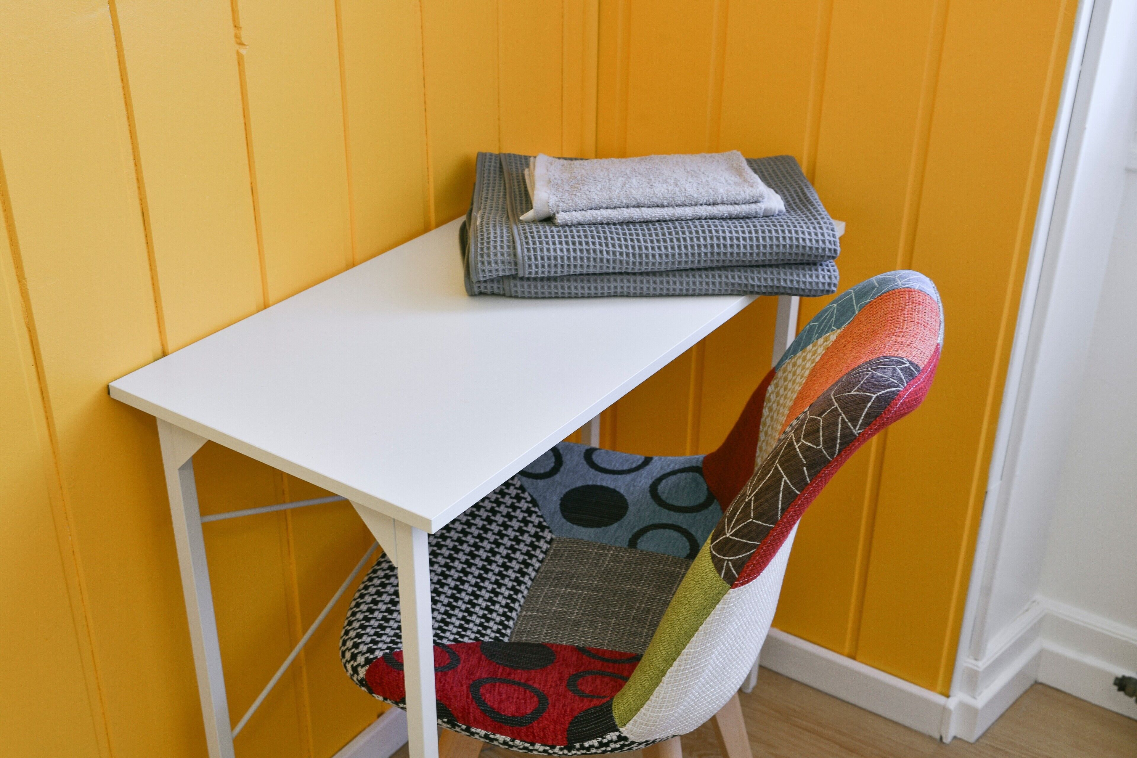 A white table with folded towels and a chair with a patchwork cushion.
