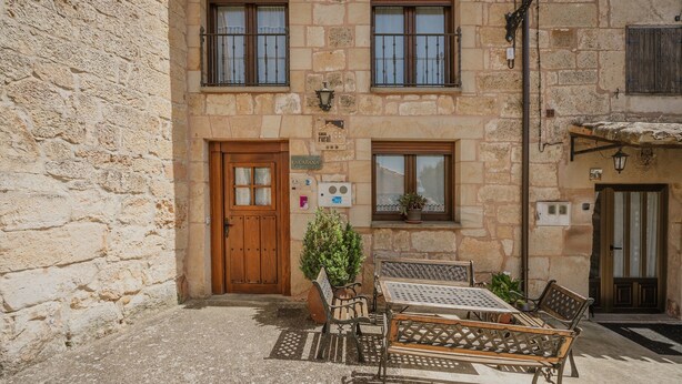 A stone building with a wooden door, a small table with chairs, and a potted plant.