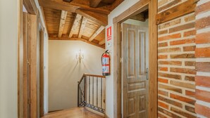 A wooden staircase with a fire extinguisher mounted on the wall, a chandelier, and a door with a brick wall.