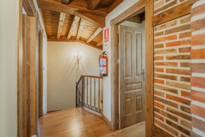 A wooden staircase with a fire extinguisher mounted on the wall, a chandelier, and a door with a brick wall.