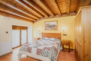 A bedroom with a wooden ceiling, a bed with a floral quilt, a wooden wardrobe, and a painting on the wall.