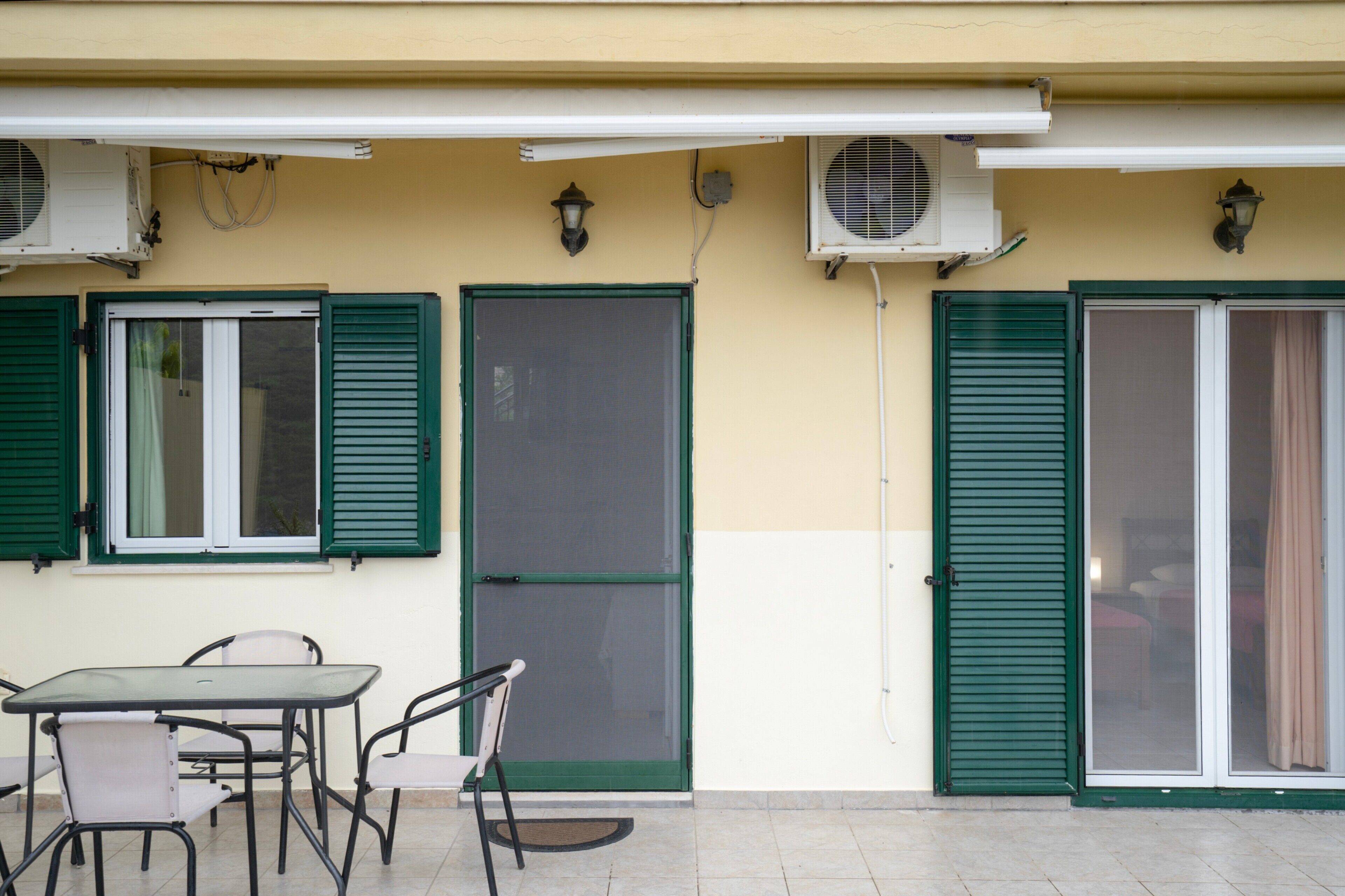 An outdoor patio with a table and chairs, a sliding glass door, and two air conditioning units mounted on the wall.