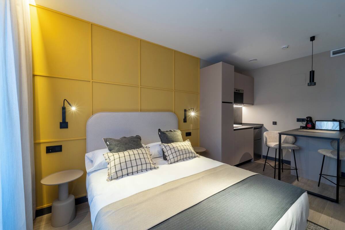 Una habitación de hotel moderna con una cama grande, una pequeña mesa redonda, una kitchenette y una zona de bar.