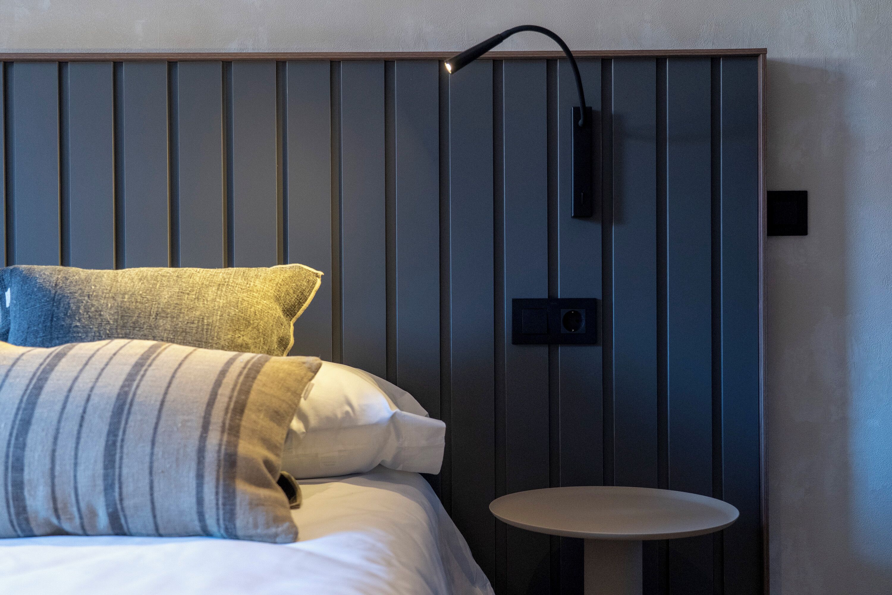 Ein modernes Hotelzimmer mit Bett, Nachttisch und Wandleuchte.