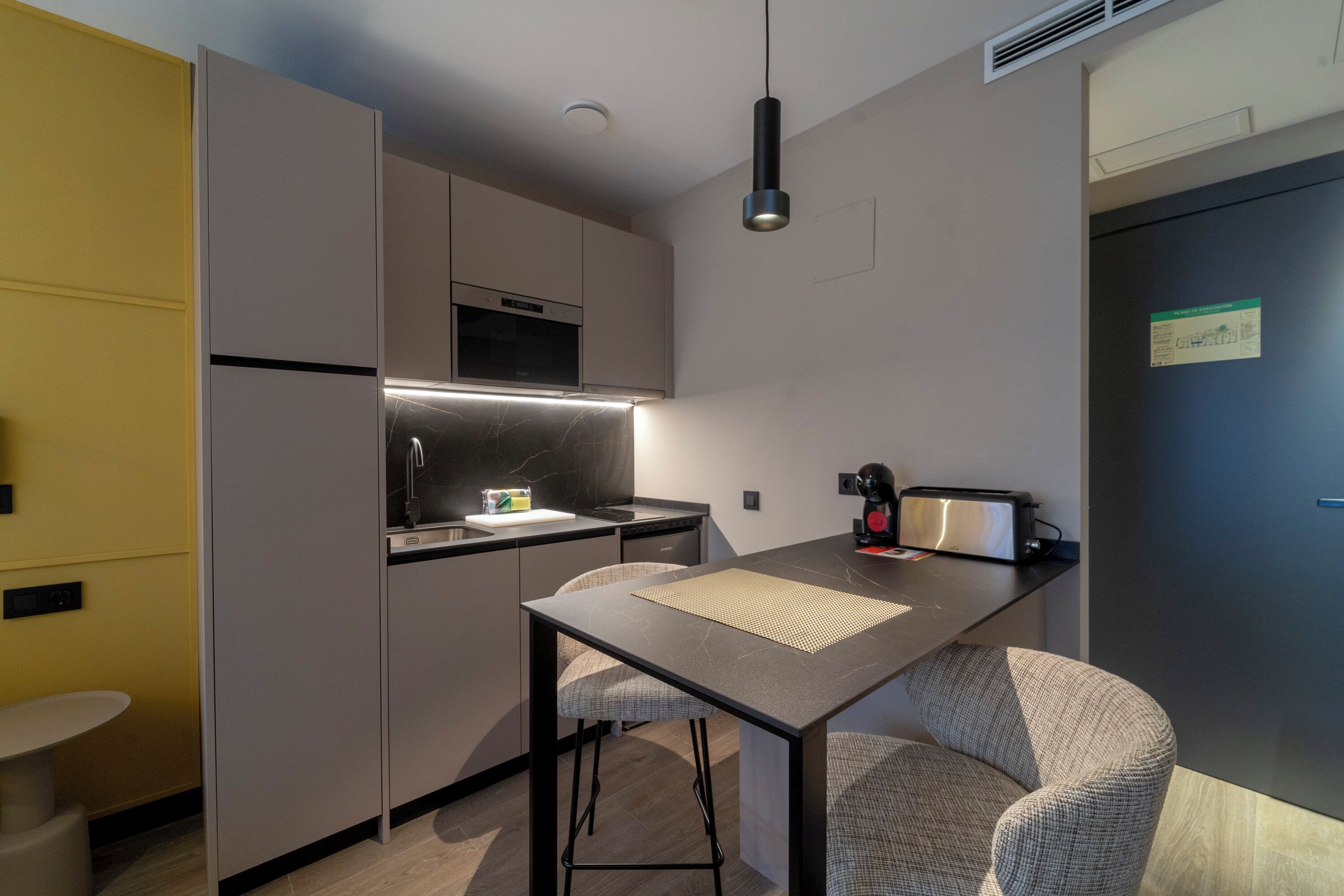 Cocina compacta con microondas, pileta y un pequeño comedor con taburetes.
