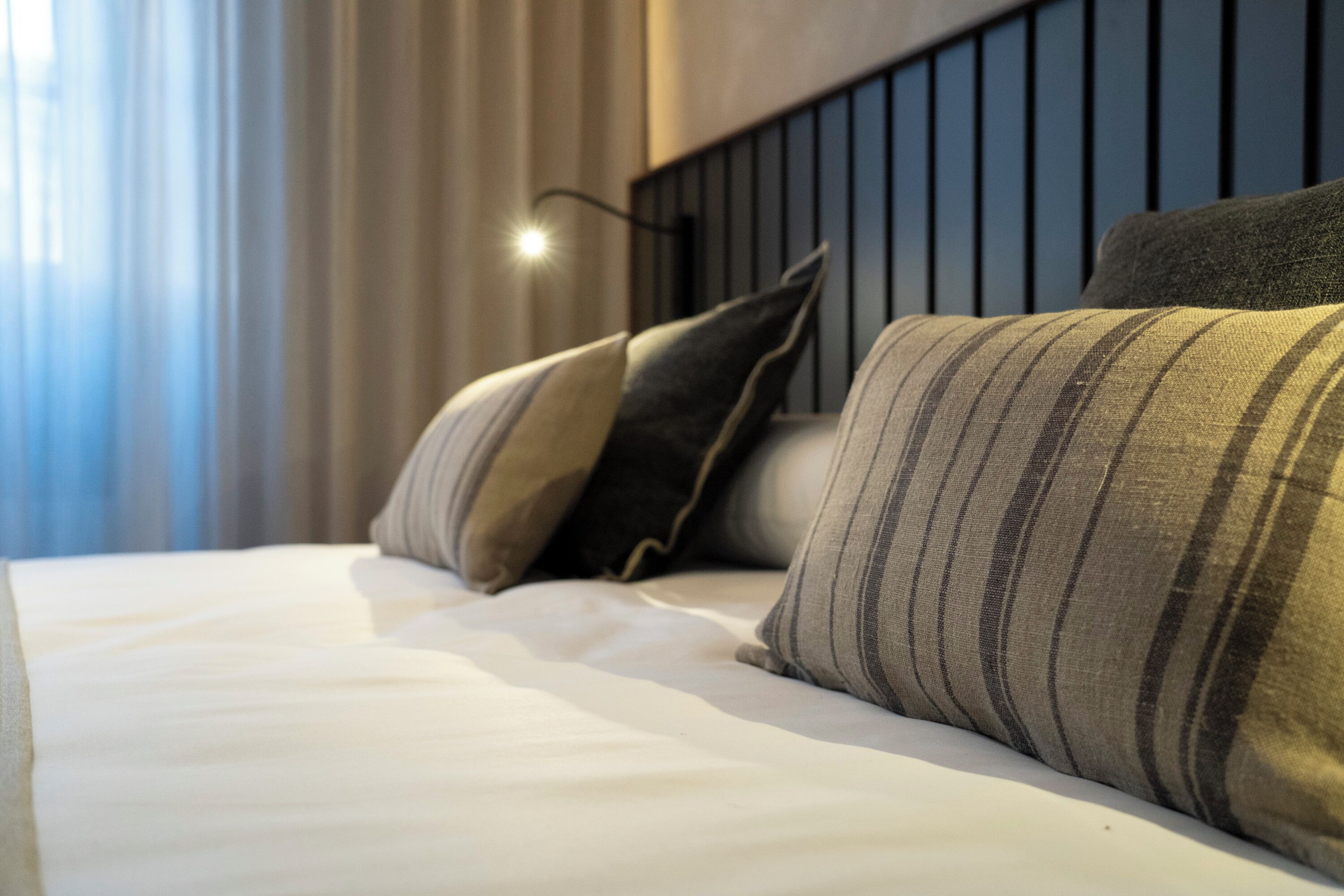 A neatly made bed with striped pillows and a headboard with vertical slats.