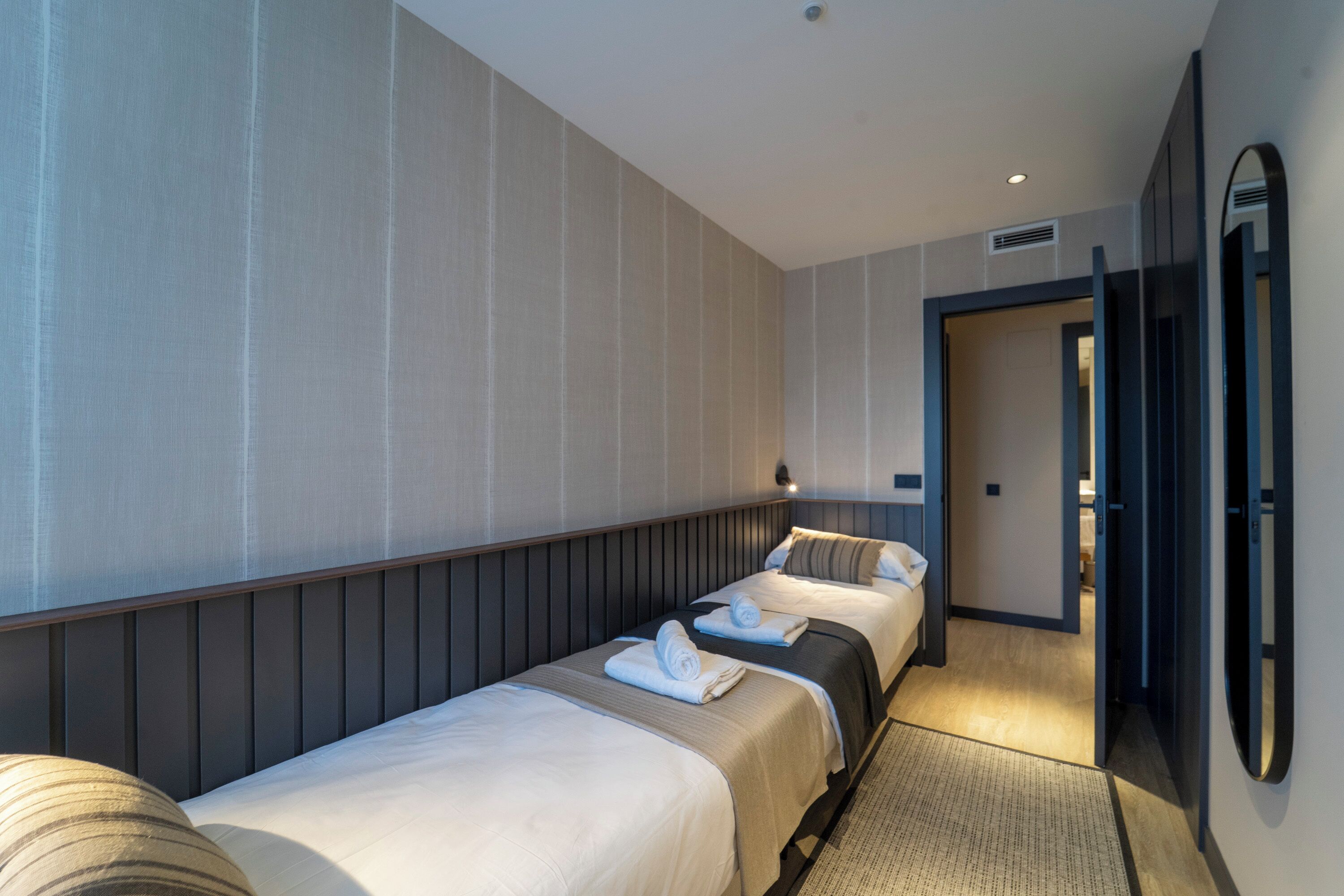 A hotel room with two beds, a large mirror, and a door leading to another room.