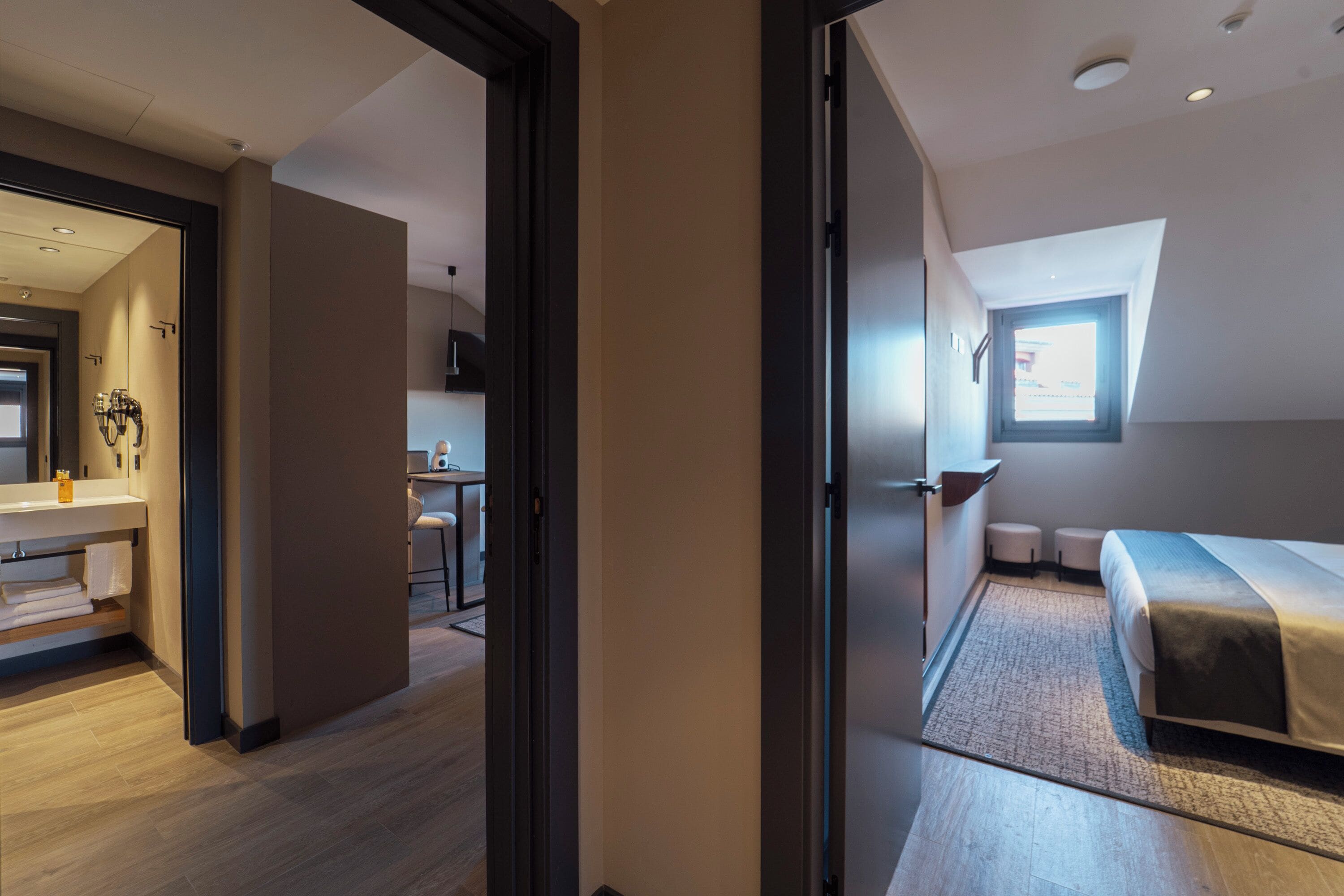 A modern hotel room with a bed, a small desk, and a kitchenette.