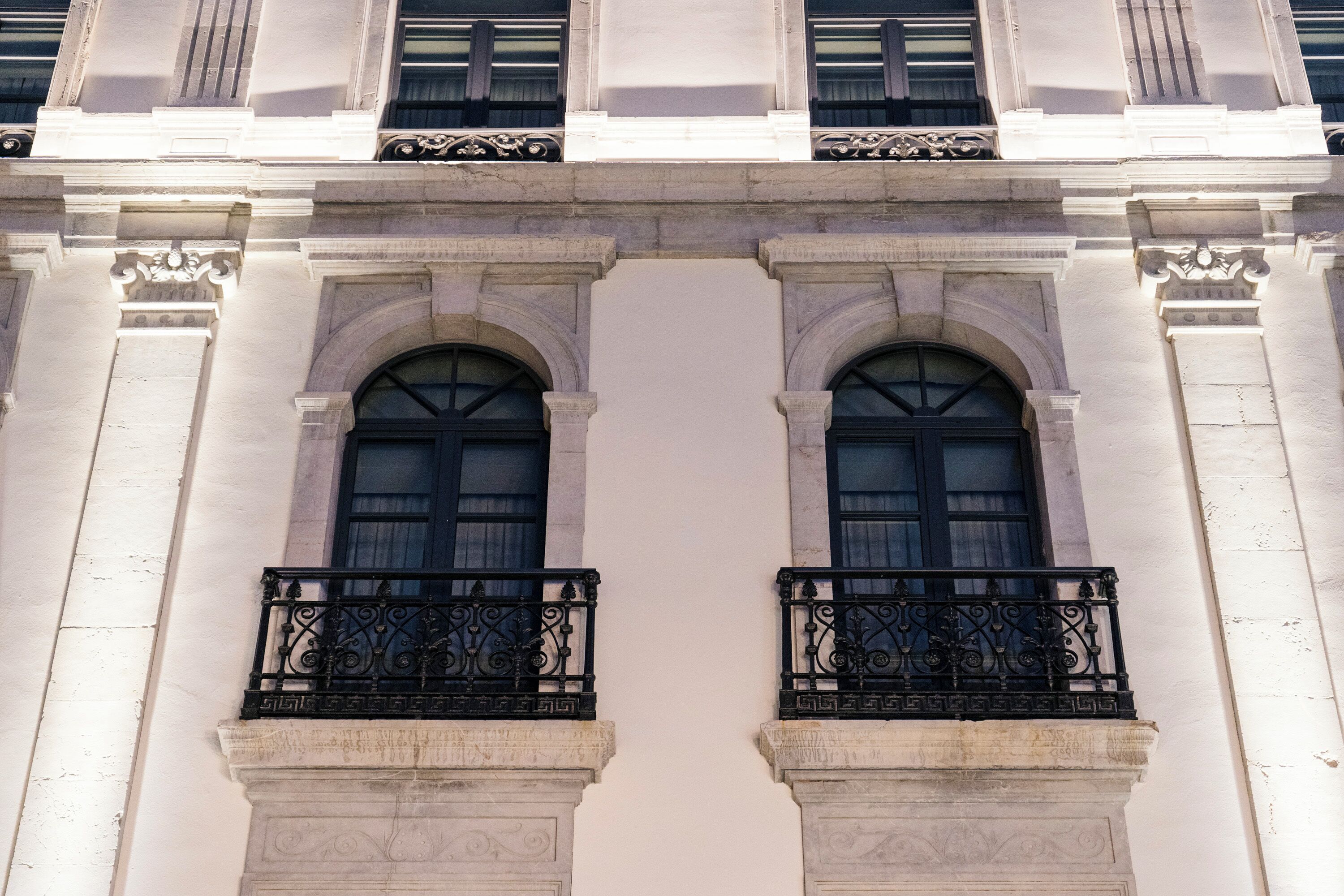 Fachada de edificio con dos ventanas arqueadas simétricas y barandillas negras ornamentales.