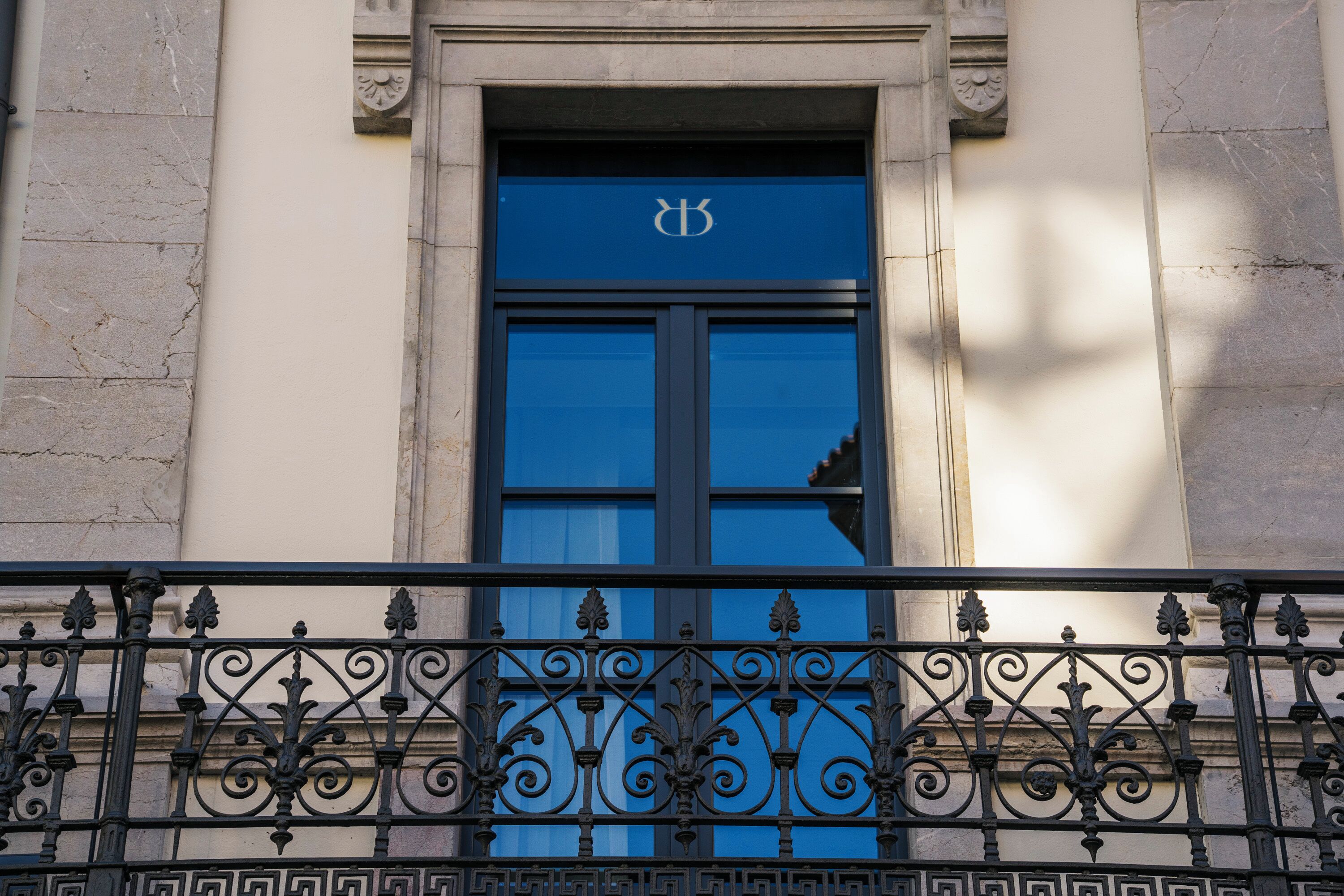 A building facade with a blue door featuring a white emblem, flanked by ornate black wrought iron railings.