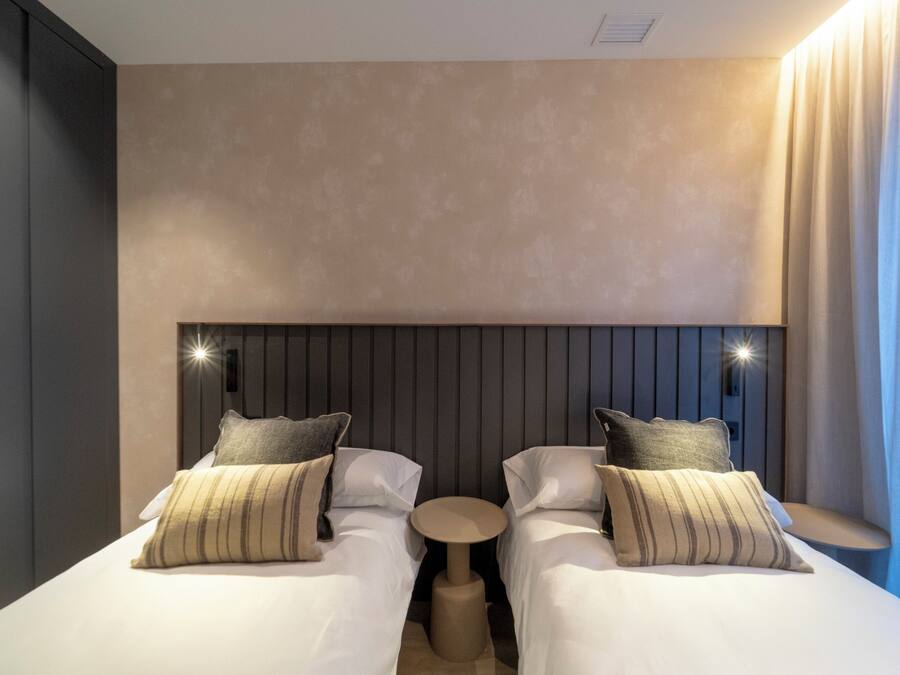 A modern hotel room with two beds, a round table, and a large headboard.