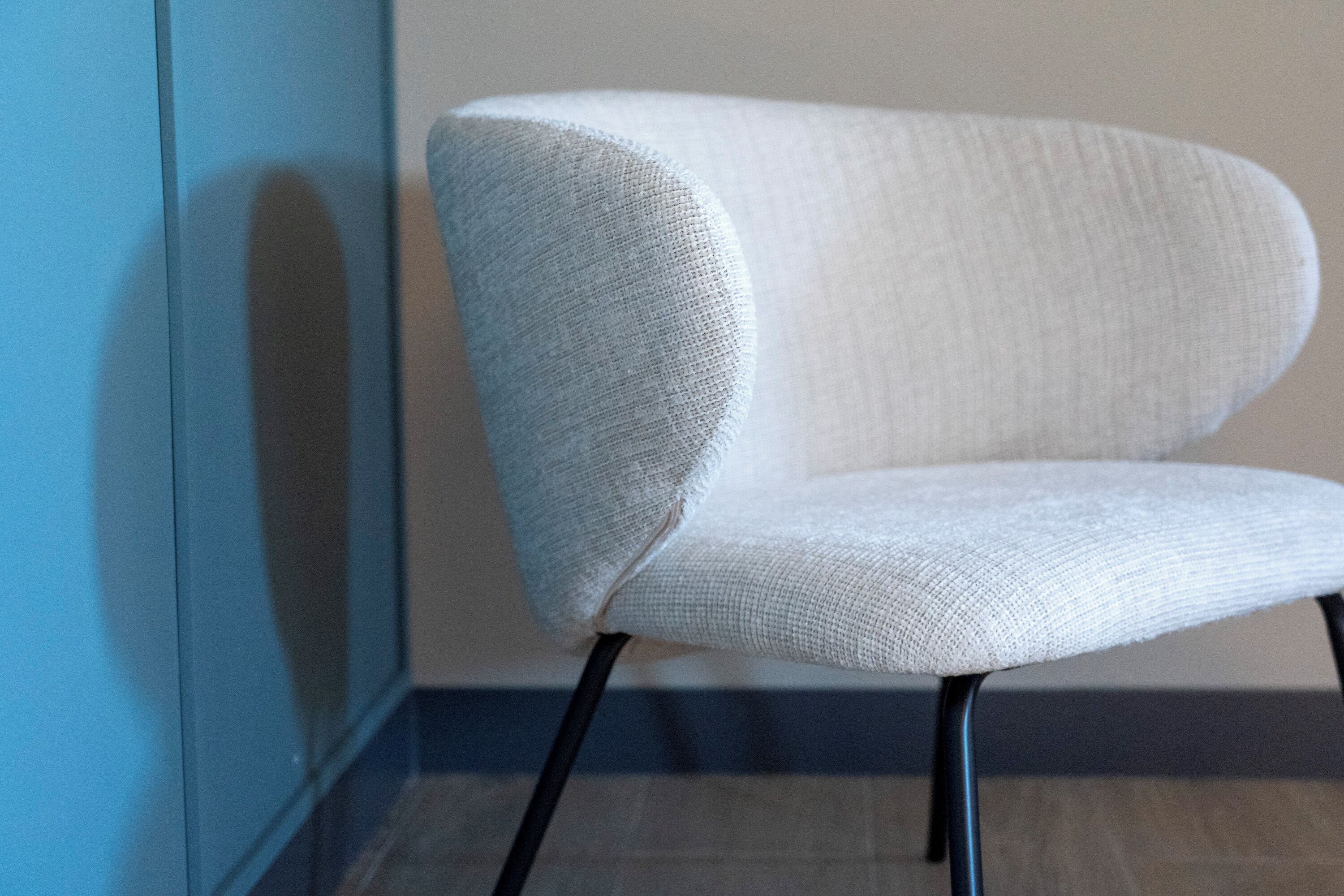 Una silla moderna con tela texturizada y patas negras, ubicada frente a una pared con decoración azul y blanca.