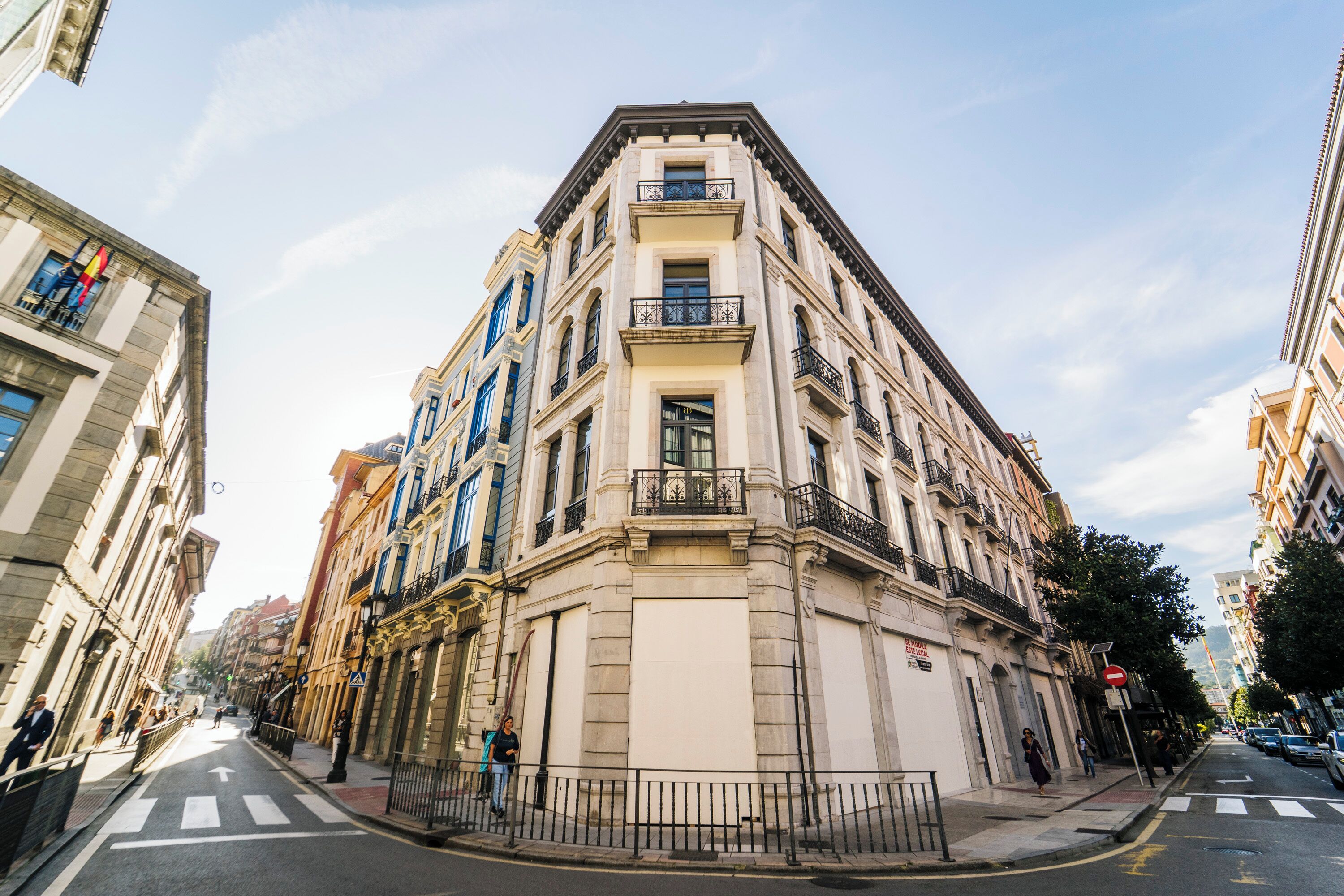 A corner building with a classical architectural style, featuring multiple floors, balconies, and a street view with a crosswalk.