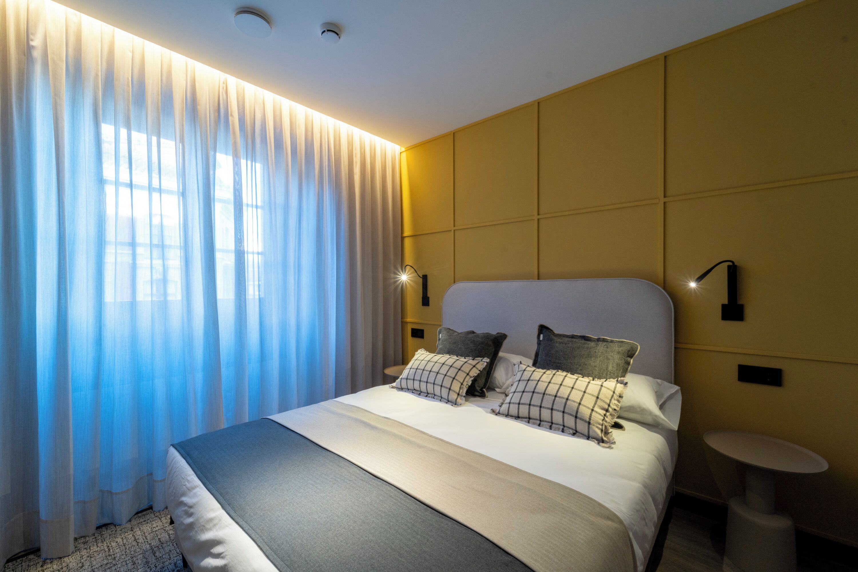 A modern hotel room with a large bed, a bedside table, and a wall-mounted lamp.