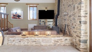 A living room with a stone wall, a flat-screen TV, a mounted clock, and a framed picture. - Country House “Le Ranch Des Ours” with Private Pool, Terrace, and Wi-Fi (Champsac)