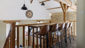 A rustic interior with exposed wooden beams, a bar area with stools, and a wall clock. - Country House “Le Ranch Des Ours” with Private Pool, Terrace, and Wi-Fi (Champsac)