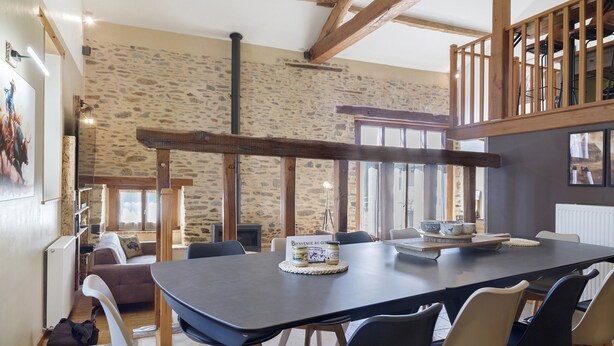 A dining area with a large table, chairs, and a rustic stone wall in the background. - Country House “Le Ranch Des Ours” with Private Pool, Terrace, and Wi-Fi (Champsac)