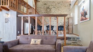 A cozy living room with a brown sofa, a wooden coffee table, and a staircase leading to a dining area. - Country House “Le Ranch Des Ours” with Private Pool, Terrace, and Wi-Fi (Champsac)