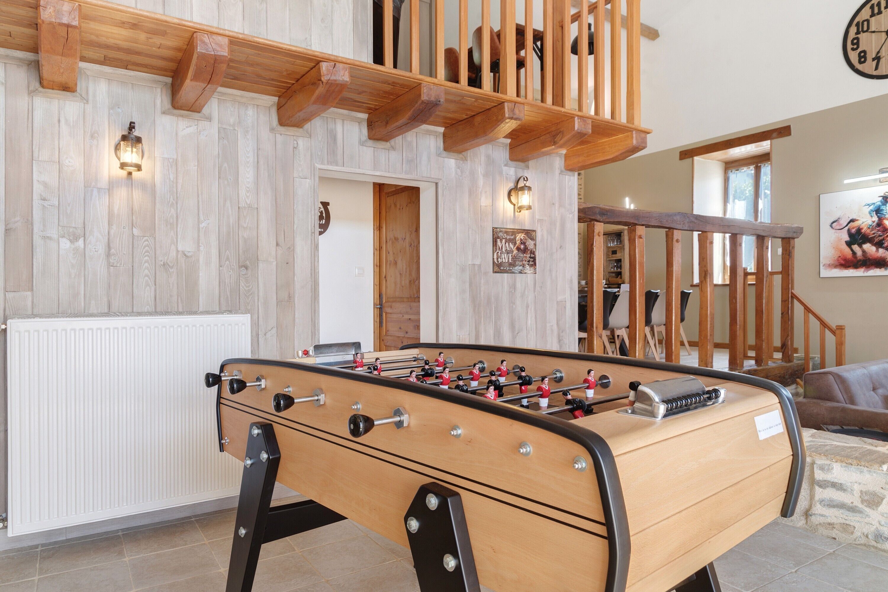 A room with a foosball table, wooden beams, a clock, and a door.